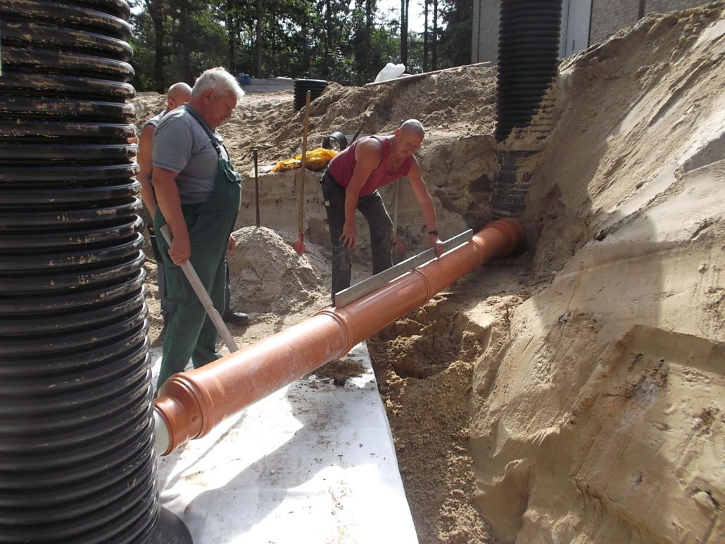 Beim Rohrleitungsbau überprüfen drei Mitarbeiter mit einer Wasserwage den Steigungswinkel
